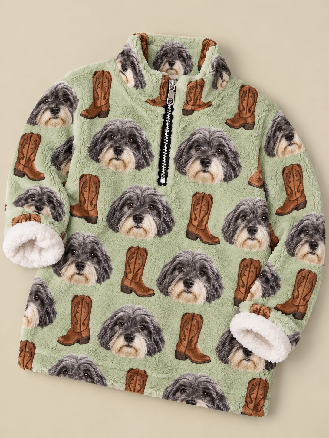 A children's fleece quarter-zip jacket featuring an all-over print of gray and white dog faces and brown cowboy boots on a light sage green background, with white sherpa-lined cuffs and collar, shown on a beige background.